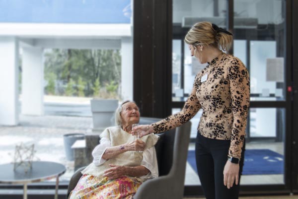 Elderly Person Receiving a Cup from Helper at Courtyard Luxury Senior Living