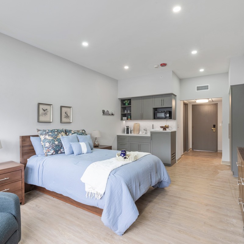 Modern bedroom with blue bedding and autumn view at Courtyard Luxury Senior Living
